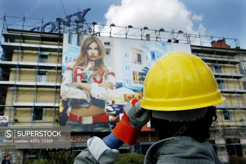 Worker at construction site looking at building with advertising poster