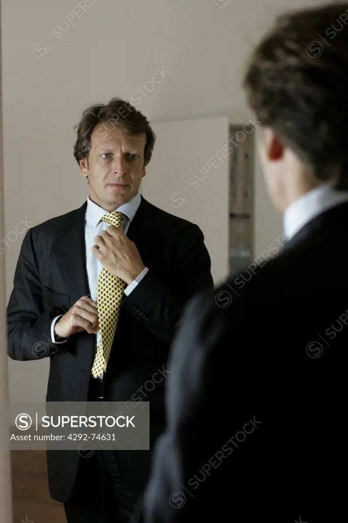 Portrait of a man doing up his tie in front of a mirror