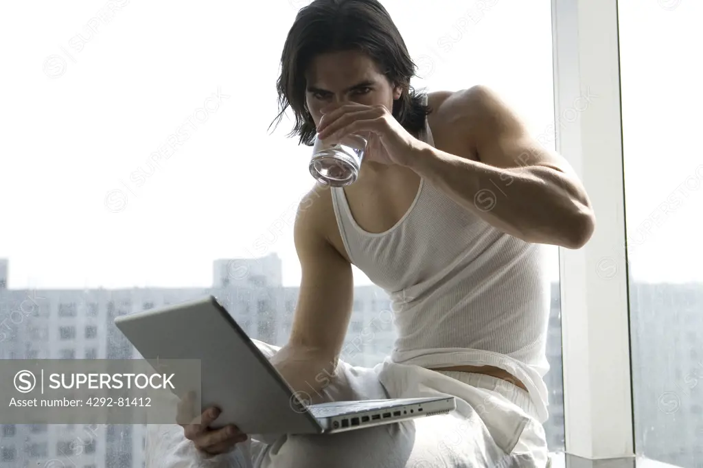 Young man with laptop drinking a glass of water