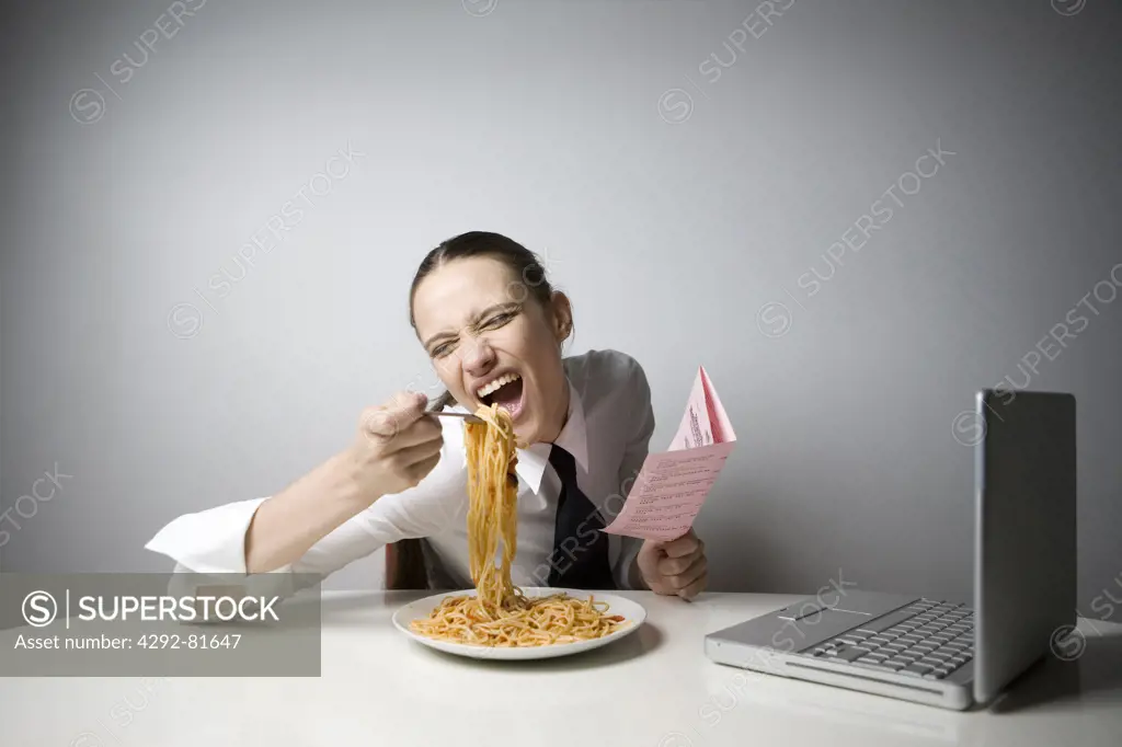 Young woman in front of laptop eating spaghetti