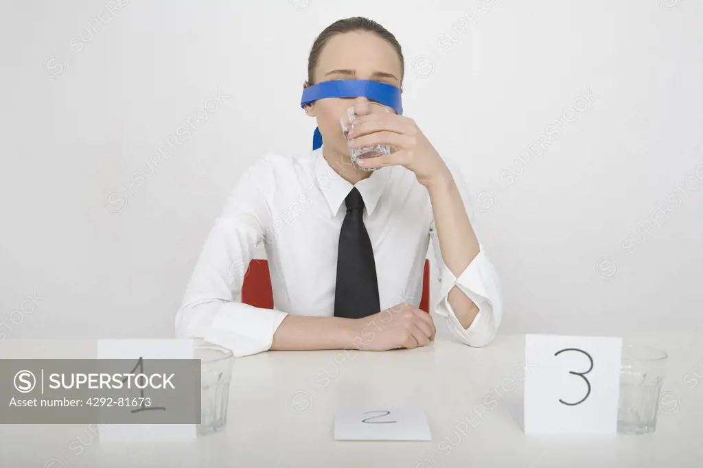 Blindfolded woman making taste test, drinking from glass