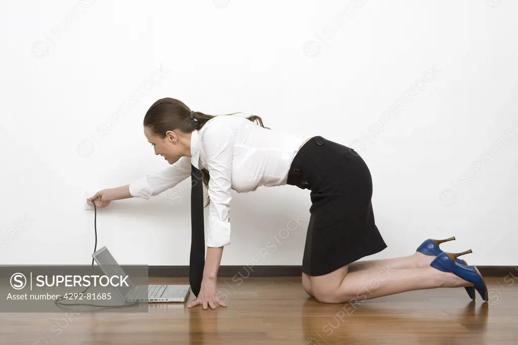 Woman kneeling on floor charging laptop