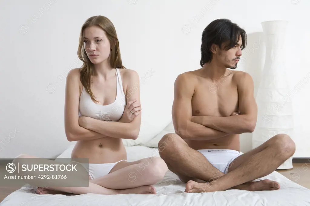 Young couple sitting on bed with arms crossed ignoring each other