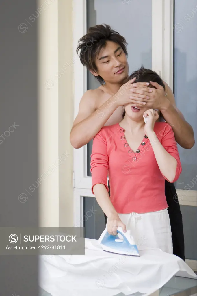 Asian man standing behind woman, covering her eyes