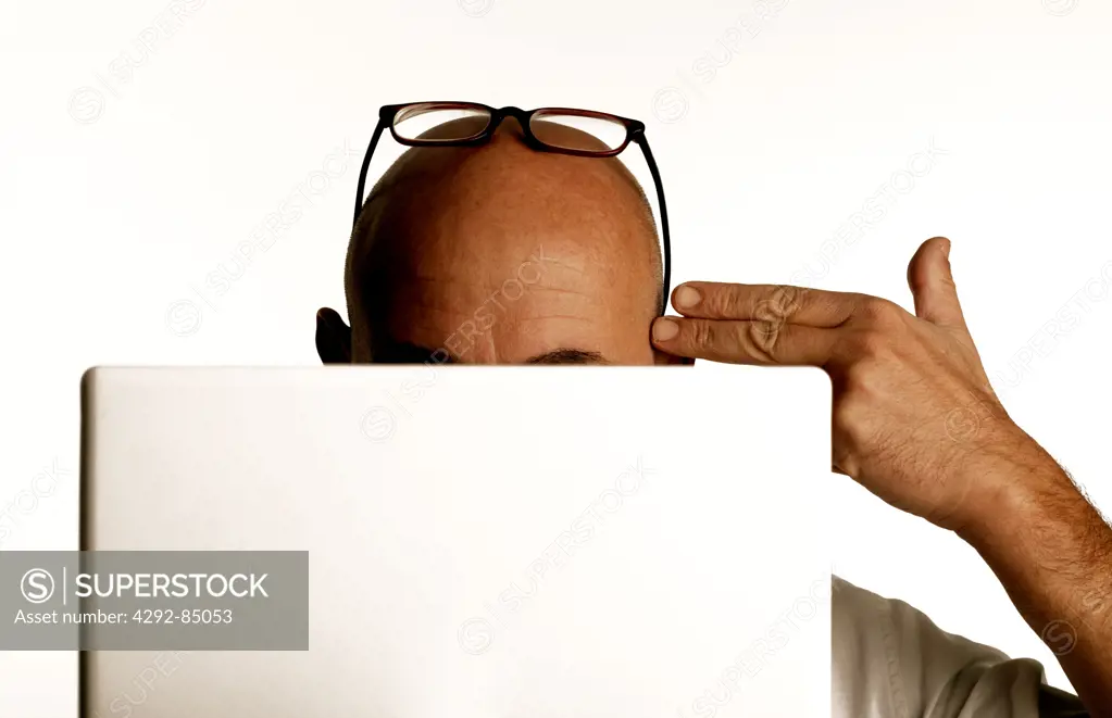 Man in front of laptop pointing at side of head