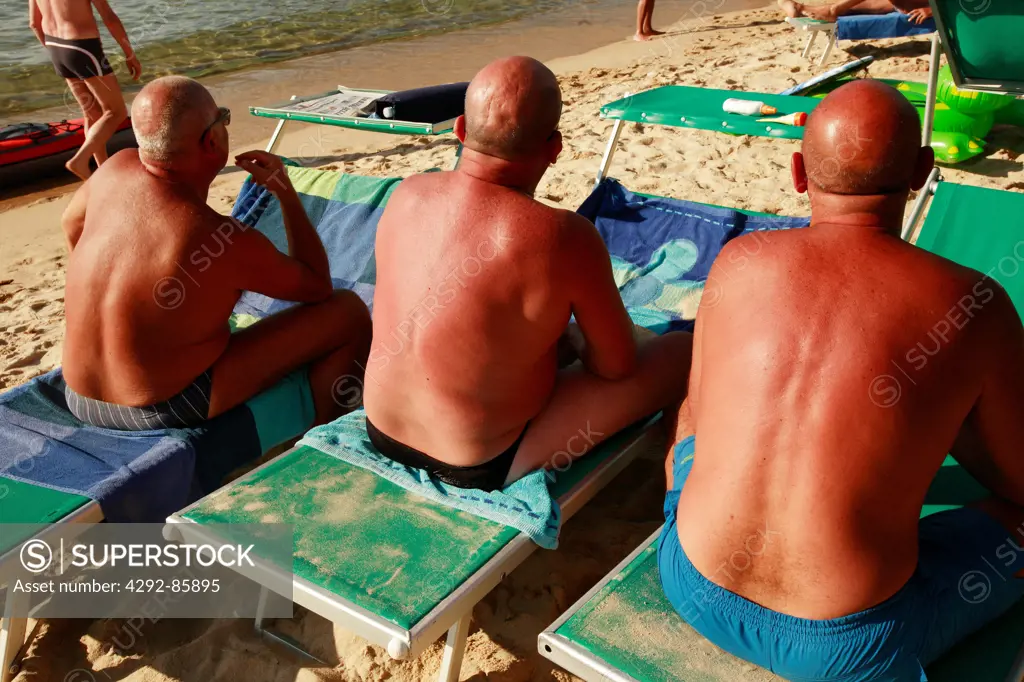 Three men at beach sitting on sunbed