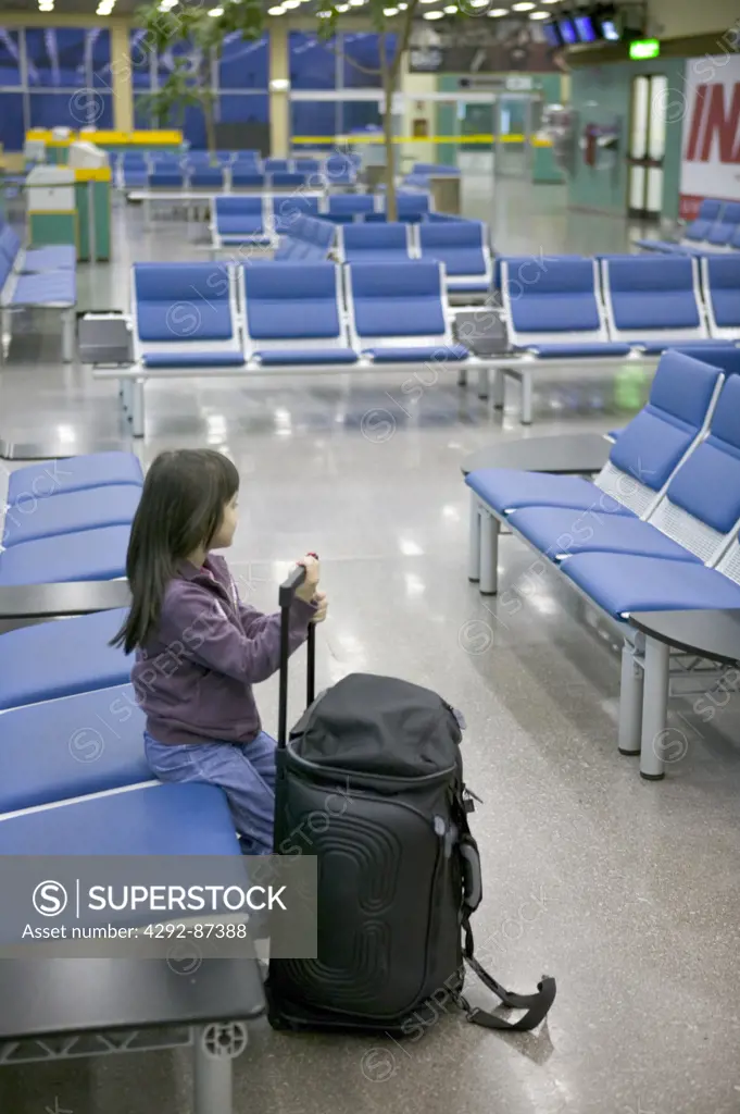 Girl sitting in airport lounge of Malpensa, with luggage Lombardy, Italy