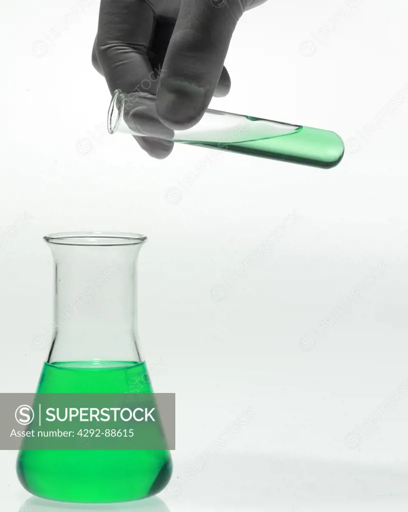 Hand of scientist with test tube pouring liquid in flask