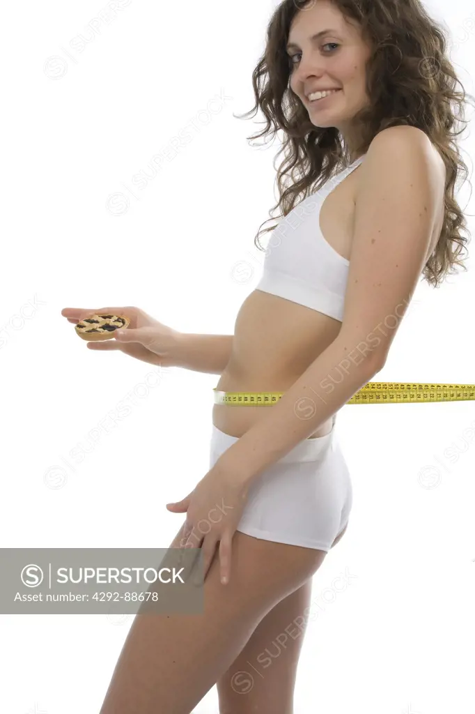 Woman measuring her waist holding a piece of cake