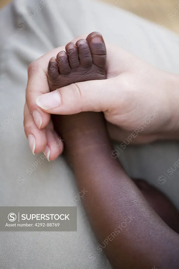 Africa, Burundi, close up of caucasian hand holding african child foot