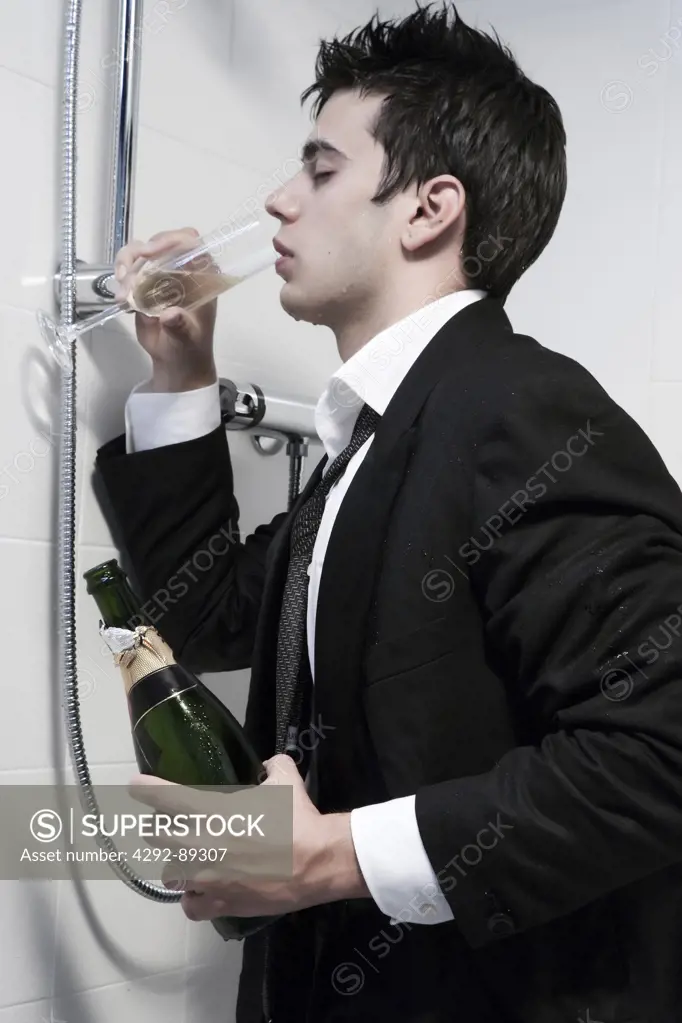 Drunk man kneeling on shower drinking from a glass