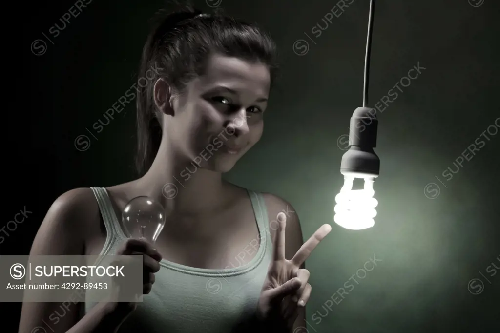 Young woman holding an old style bulband pointing at energy efficient lightbulb