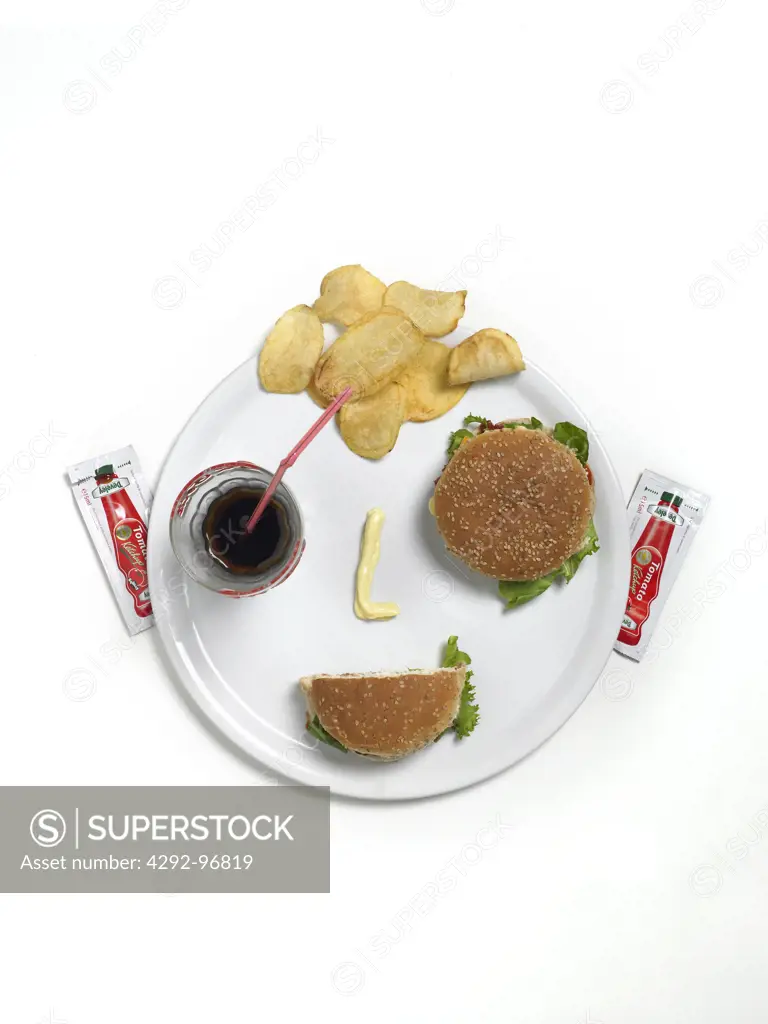 Hamburgers, potato chips and  coca cola glass on dish shaped as human face