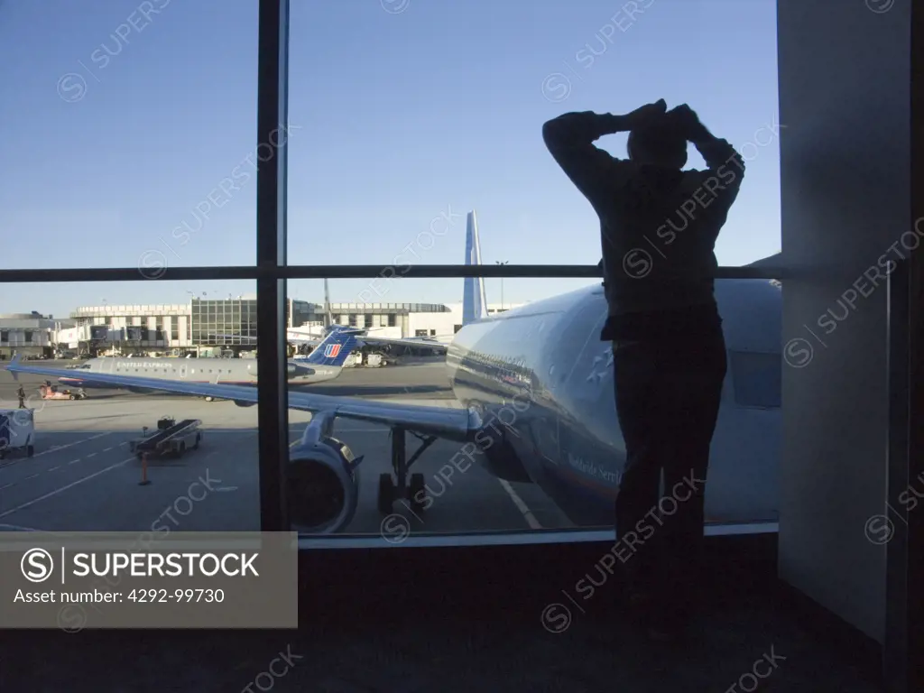 Silhouette of a man in airport in front of window, airplane in background