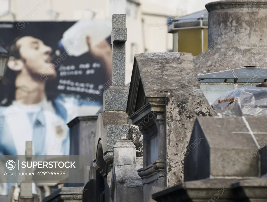 Gravestones in La Recoleta Cemetery in Buenos Aires, Argentina contrast with nearby advertising.