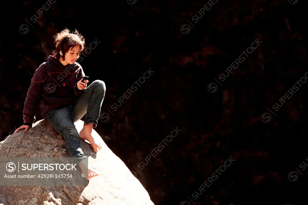 Boy sitting on stream rock listening to music