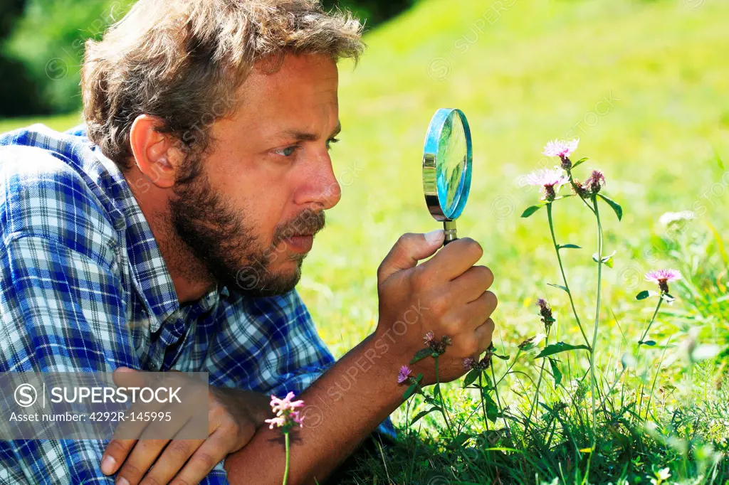 Young man with magnifying glass looking at flower