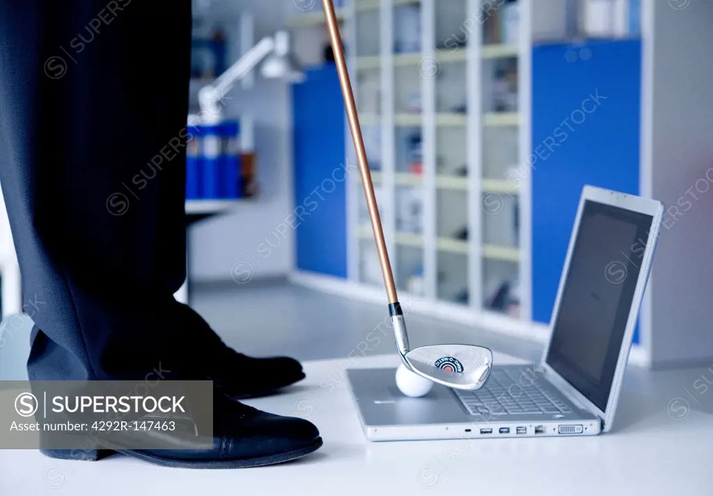Businessman in front of laptop with golf club
