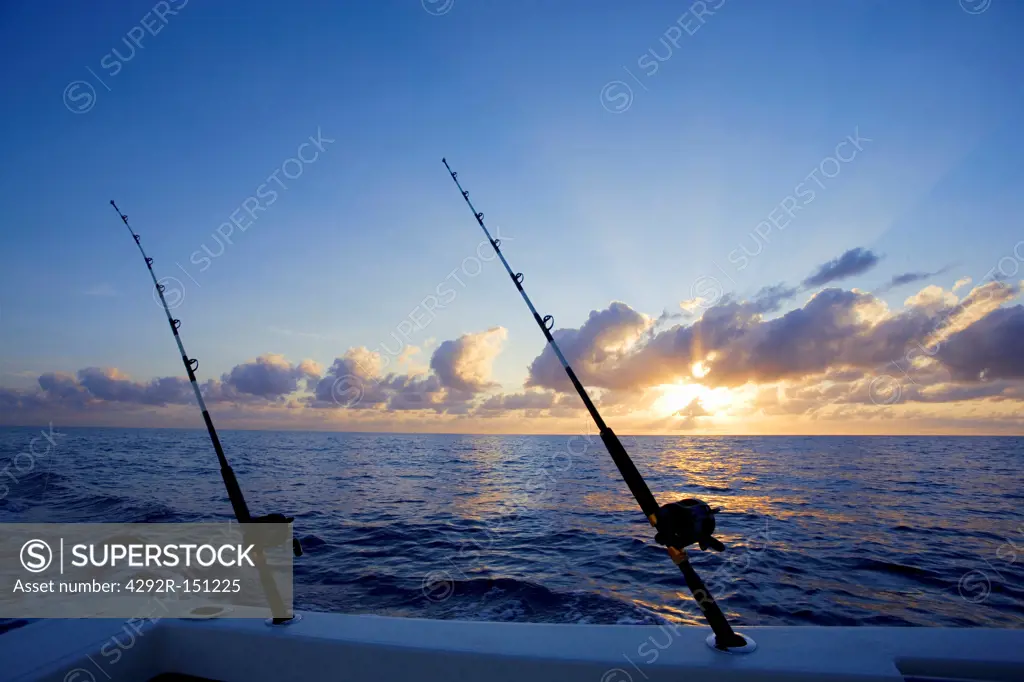Fishing rods on boat with sunrise over the ocean in background, Florida, USA
