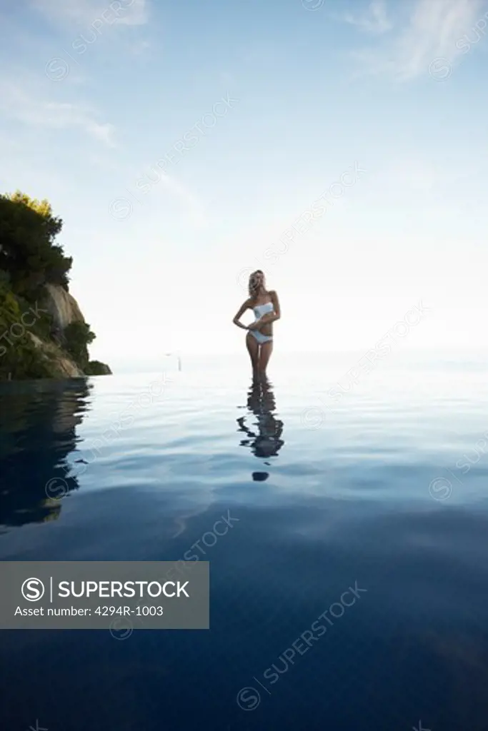 Young woman in monokini standing in infinity pool