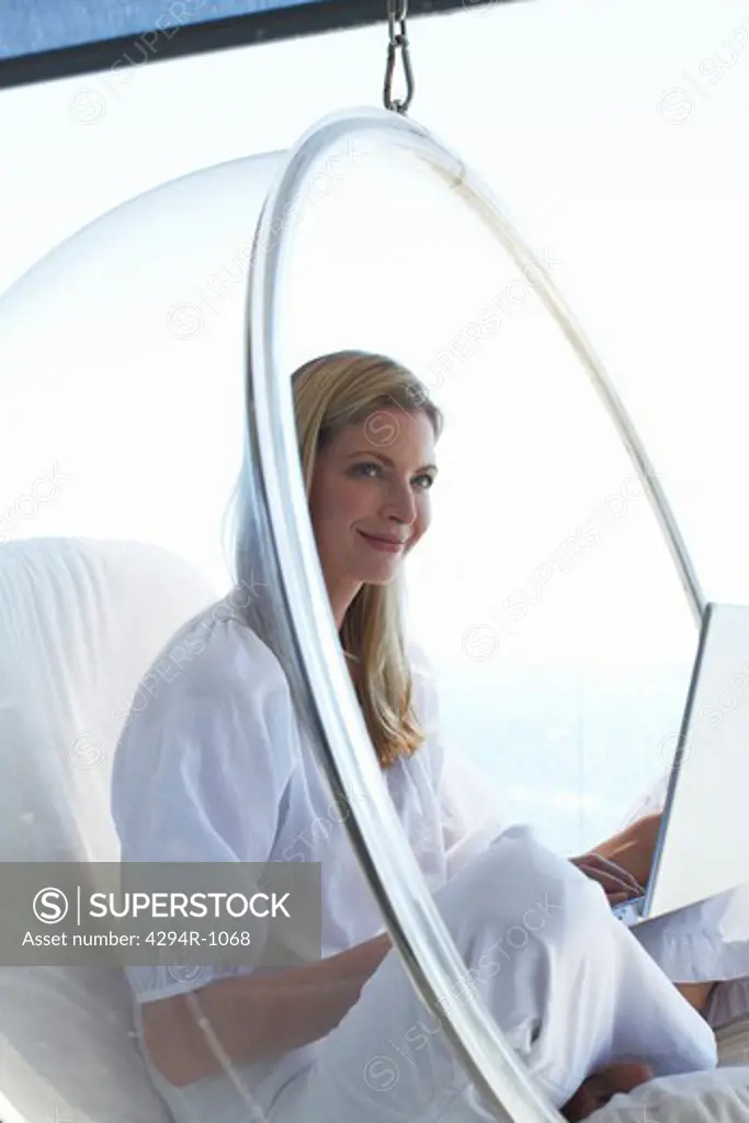 Smiling woman using laptop in hanging chair