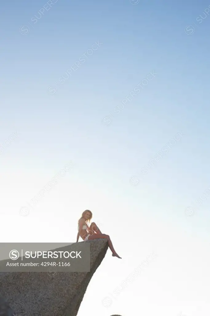 Young woman sitting on rock under blue sky