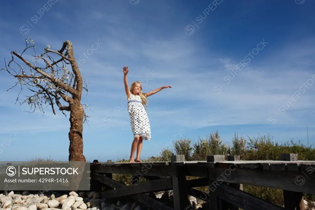 Girl standing on wooden path with arms outstretched