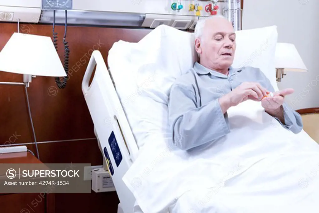 Senior man in hospital bed taking pills