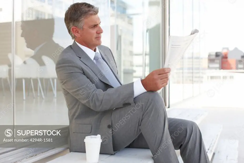 Businessman reading newspaper outside office