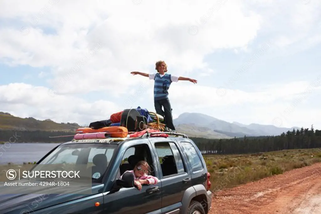 Boy balancing on car roof in remote landscape
