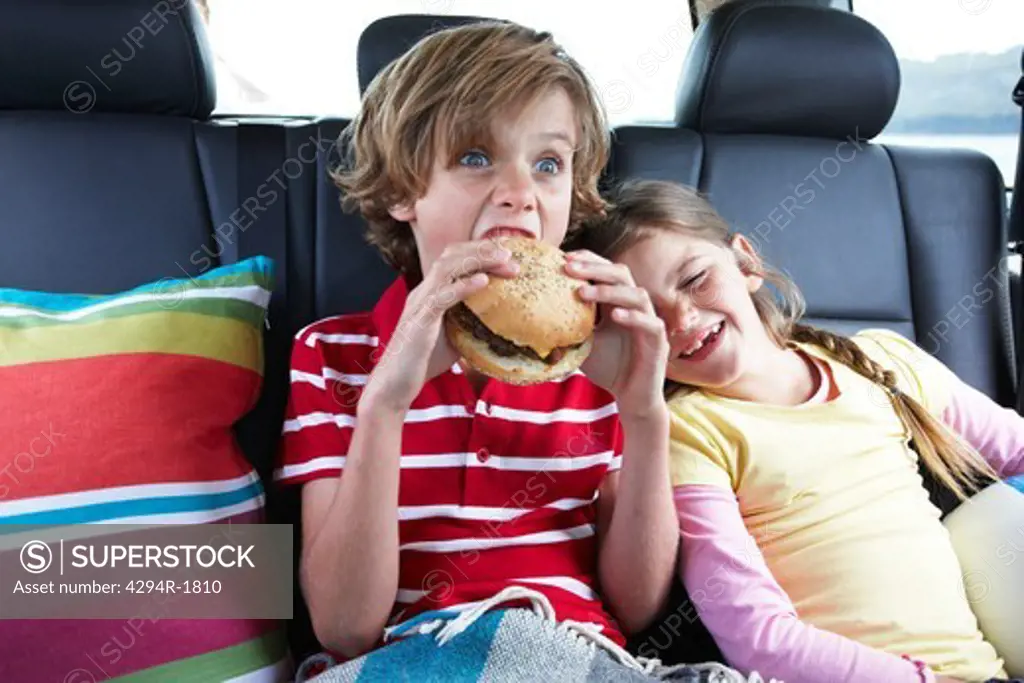 Brother and sister eating hamburger in the back of a car