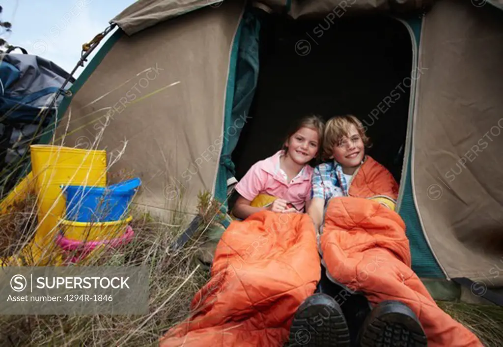 Brother and sister with sleeping bags in a tent