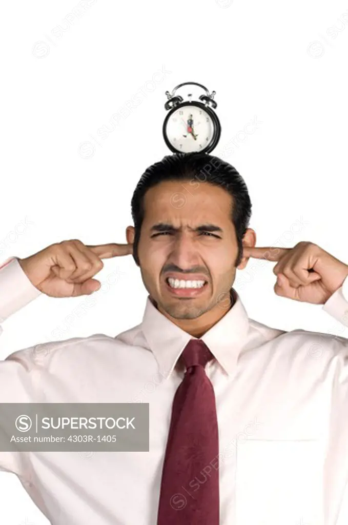 Businessman with alarm clock on head and fingers in ears