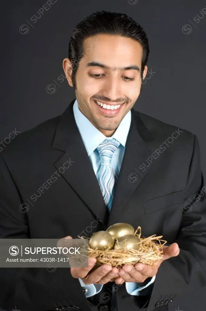 Businessman holding nest with golden egg, smiling