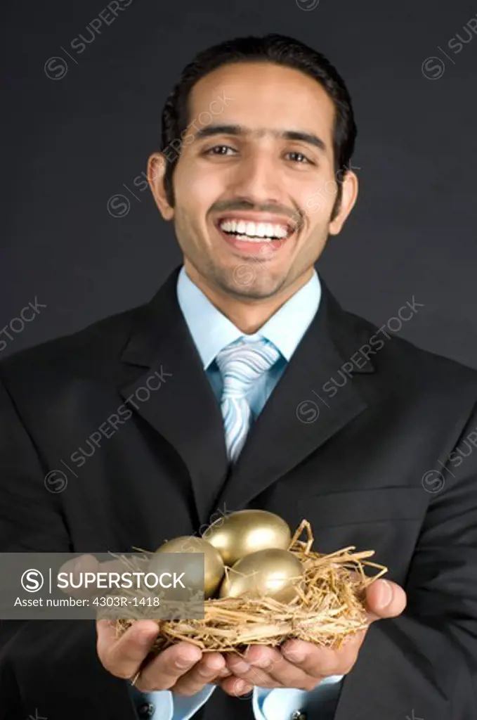 Businessman holding nest with golden egg, smiling, portrait