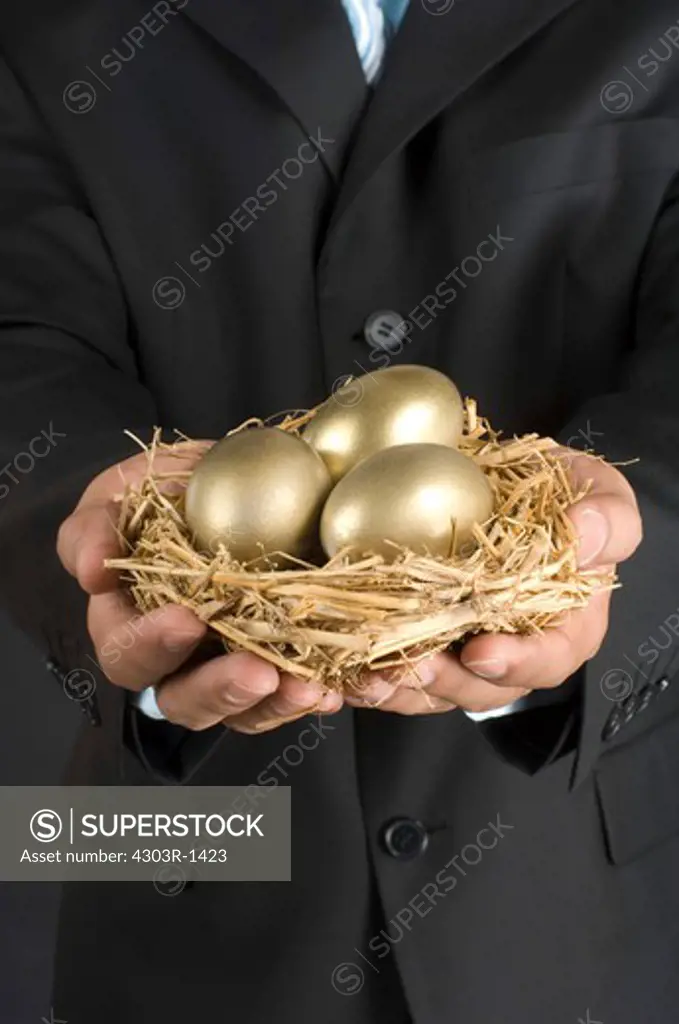 Businessman holding nest with golden egg, midsection