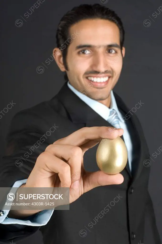 Businessman holding golden egg, smiling, portrait