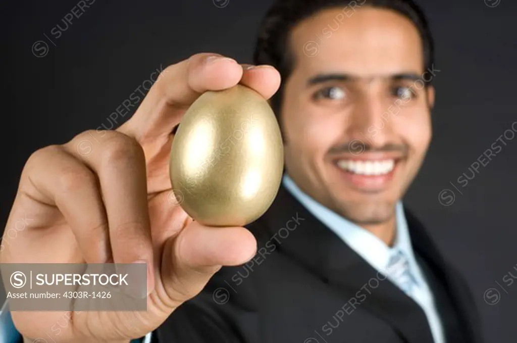 Businessman holding golden egg, smiling