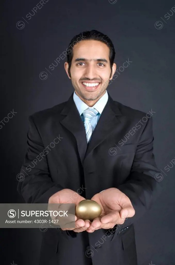 Businessman holding golden egg in cupped hand, smiling, portrait