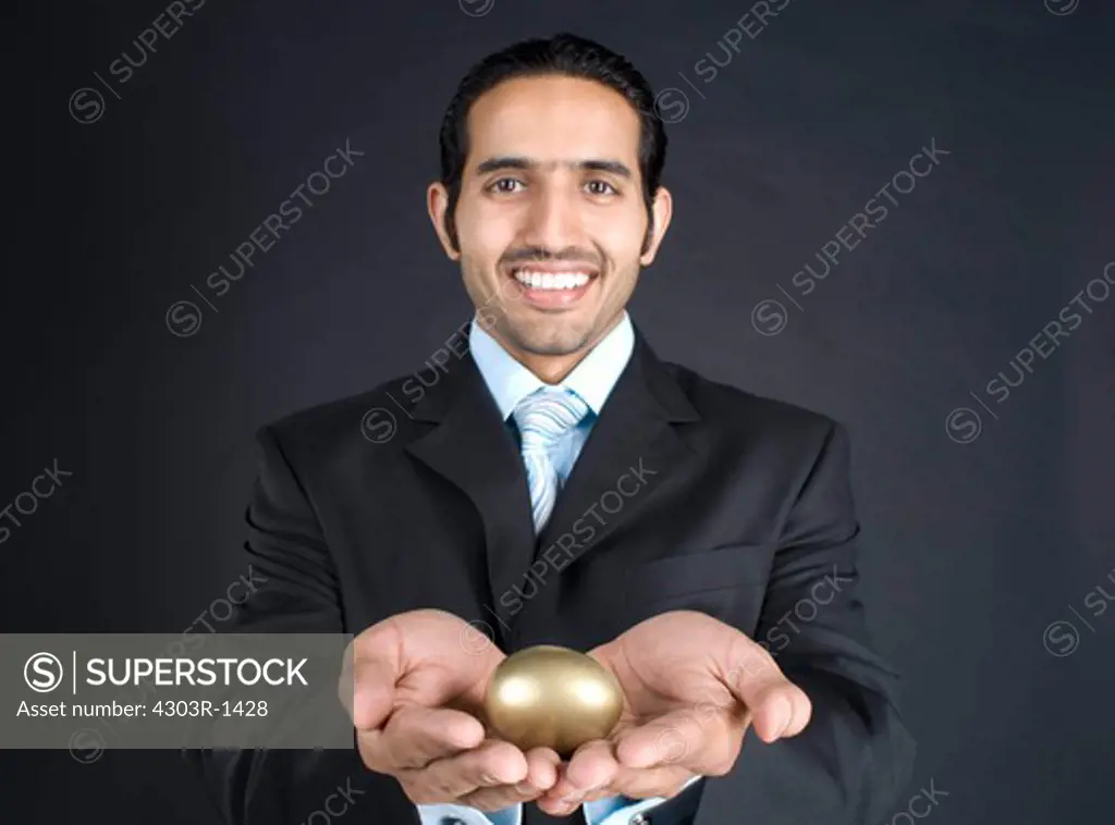 Businessman holding golden egg, smiling, portrait