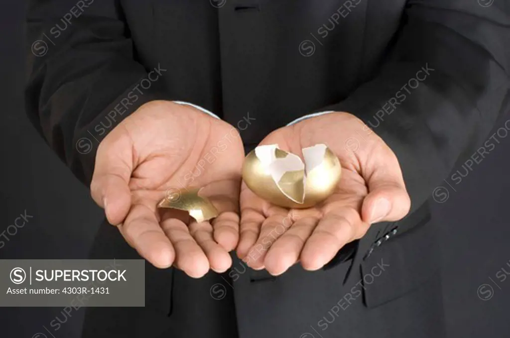 Businessman holding broken golden egg in cupped hand, midsection