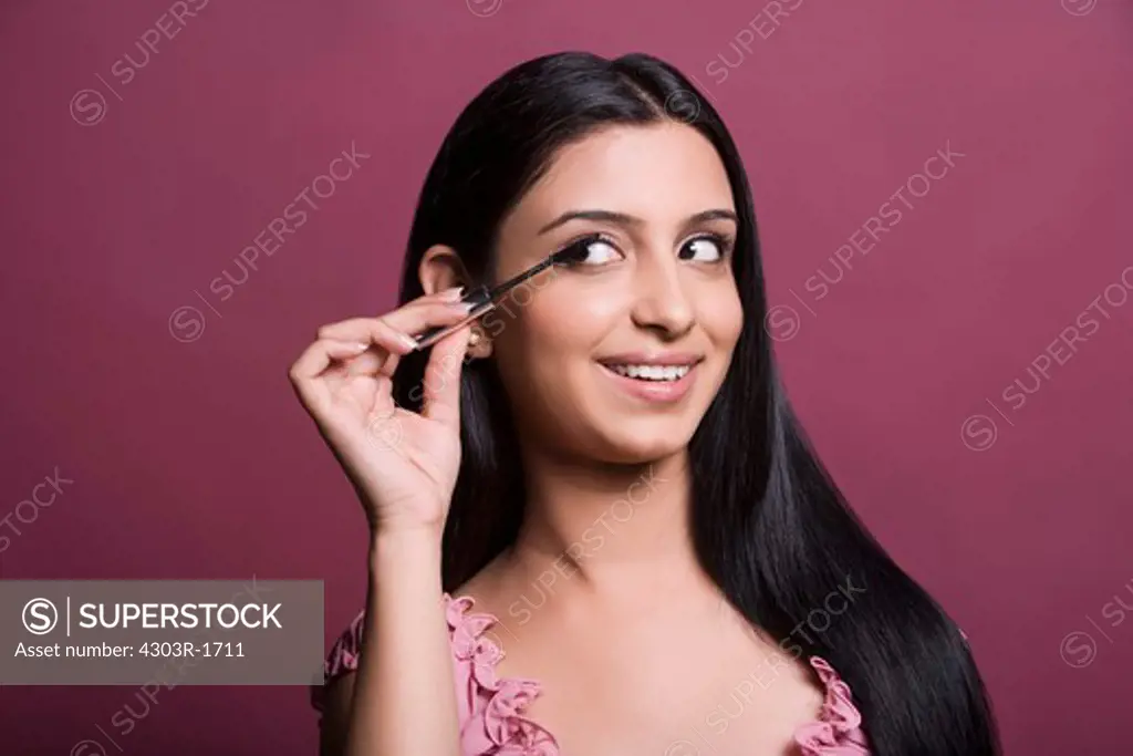 Young woman applying mascara, smiling