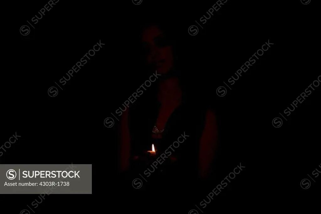 Young woman holding candle in dark