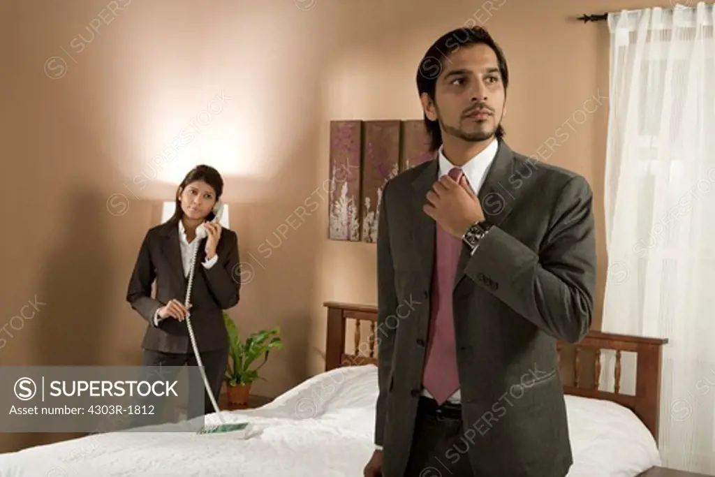 Businessman adjusting tie with woman on phone in background