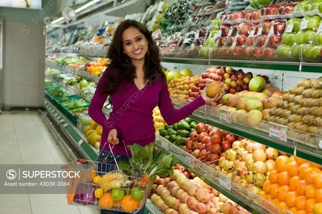 Mid adult woman holding shopping basket at supermarket, portrait