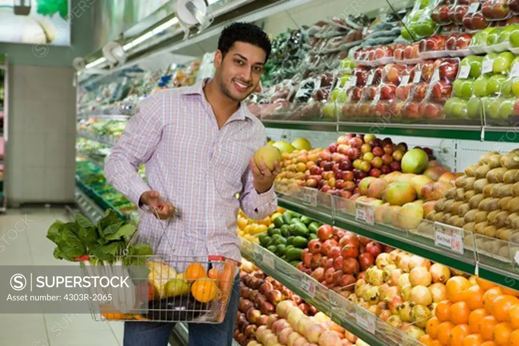 Mid adult man holding shopping basket at supermarket, portrait