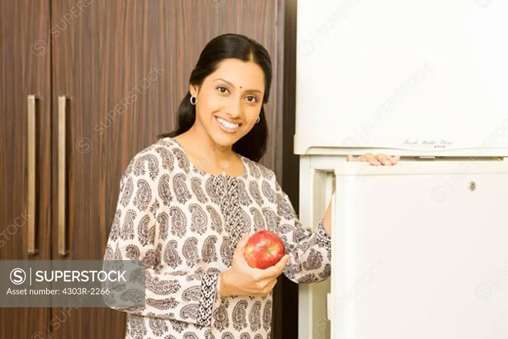 Woman in front of the refrigerator holding an red apple