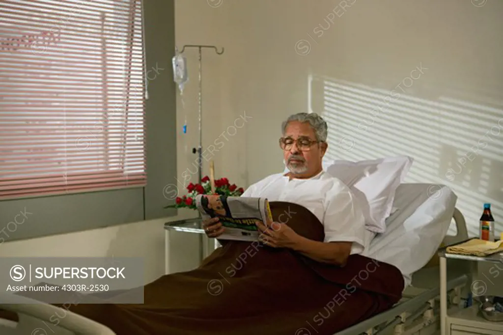 Old man patient reading newspaper while in hospital bed