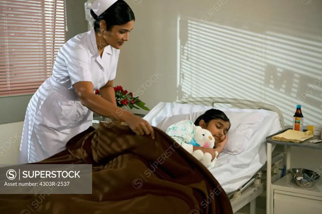 Female nurse putting a blanket on a sleeping girl in a hospital