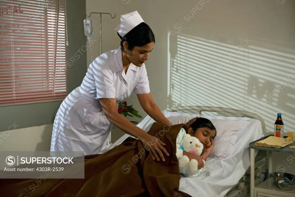 Female nurse putting a blanket on a sleeping girl in a hospital